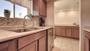 A kitchen with a double sink, wooden cabinets, a tiled backsplash, and a window with a plant.