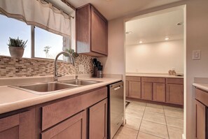A kitchen with a double sink, wooden cabinets, a tiled backsplash, and a window with a plant. - Walkable Old Town 2BD 2BA Retreat Camelback Views Pools BBQs (Scottsdale)