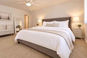 A bedroom with a large bed, bedside tables, a ceiling fan, and a door leading to another room.
