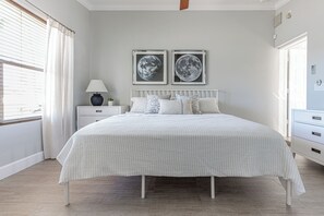 Een slaapkamer met een bed, nachtkastje, lamp en twee ingekaderde foto’s aan de muur.