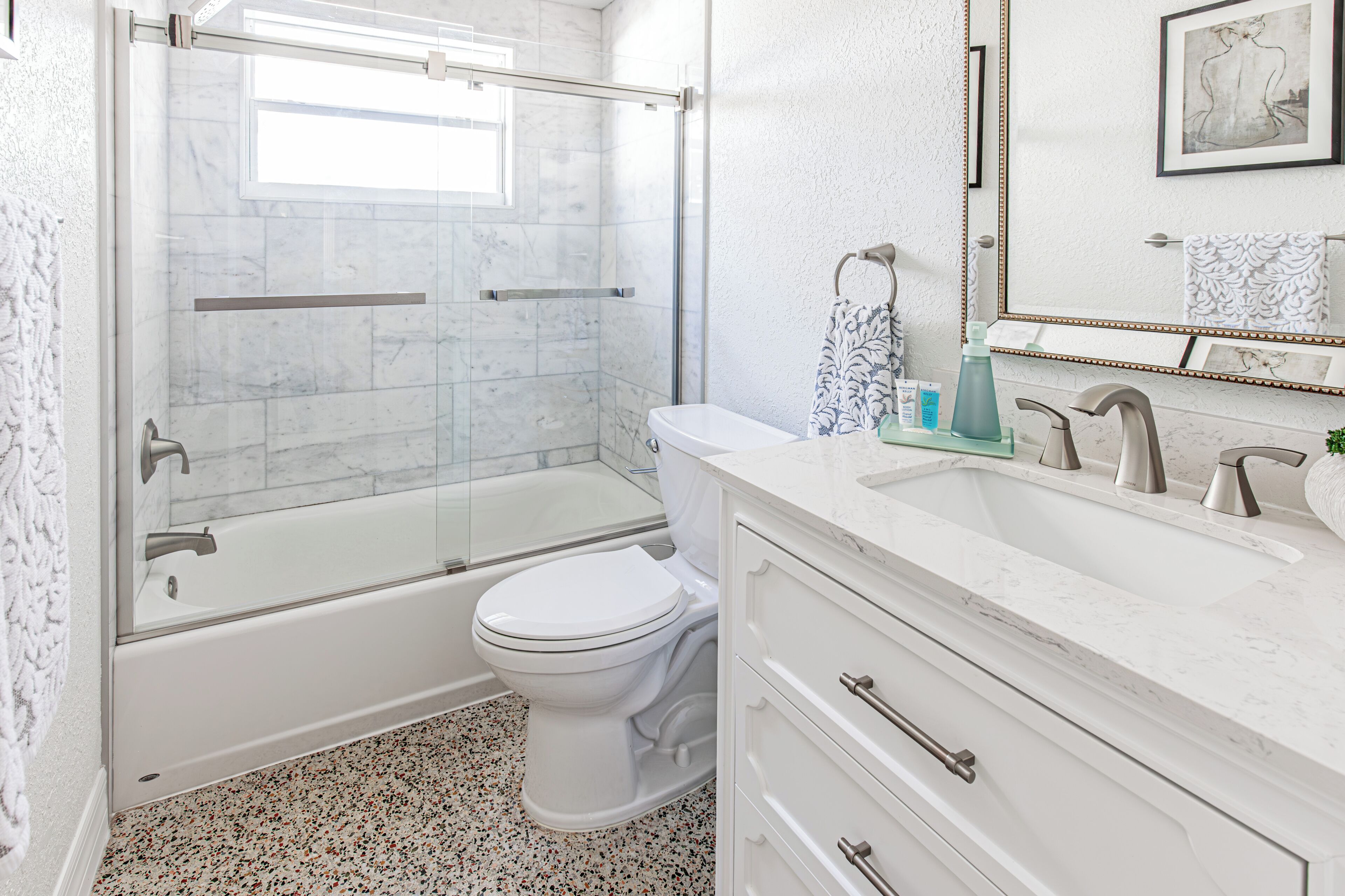 A bathroom with a glass-enclosed shower, a toilet, a sink with a mirror, and a vanity with drawers.
