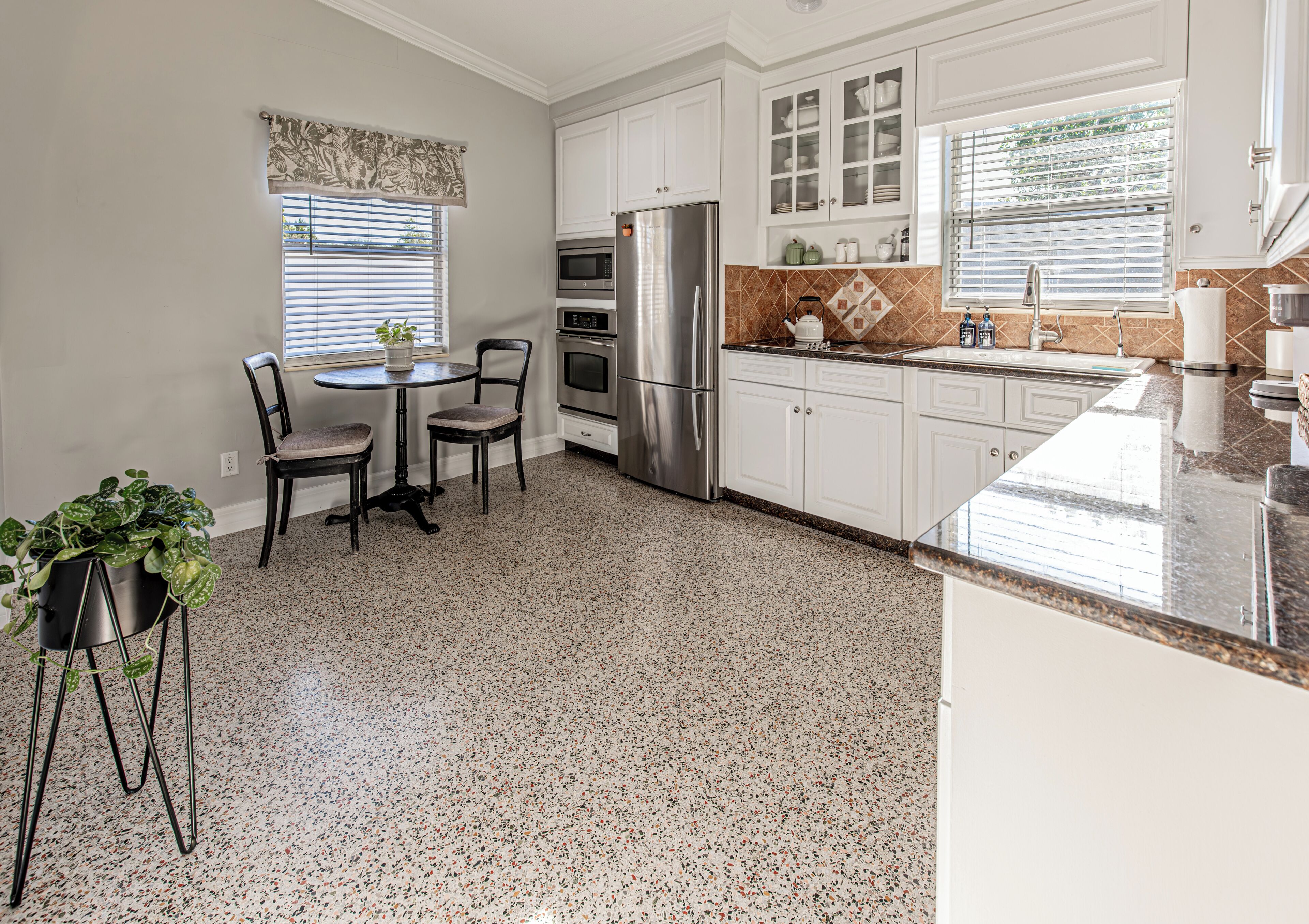 A kitchen with white cabinets, a stainless steel refrigerator, a microwave, and a granite countertop.