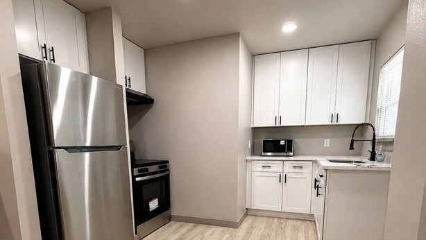 Una cocina moderna con gabinetes blancos, un refrigerador de acero inoxidable, un microondas y un lavamanos.