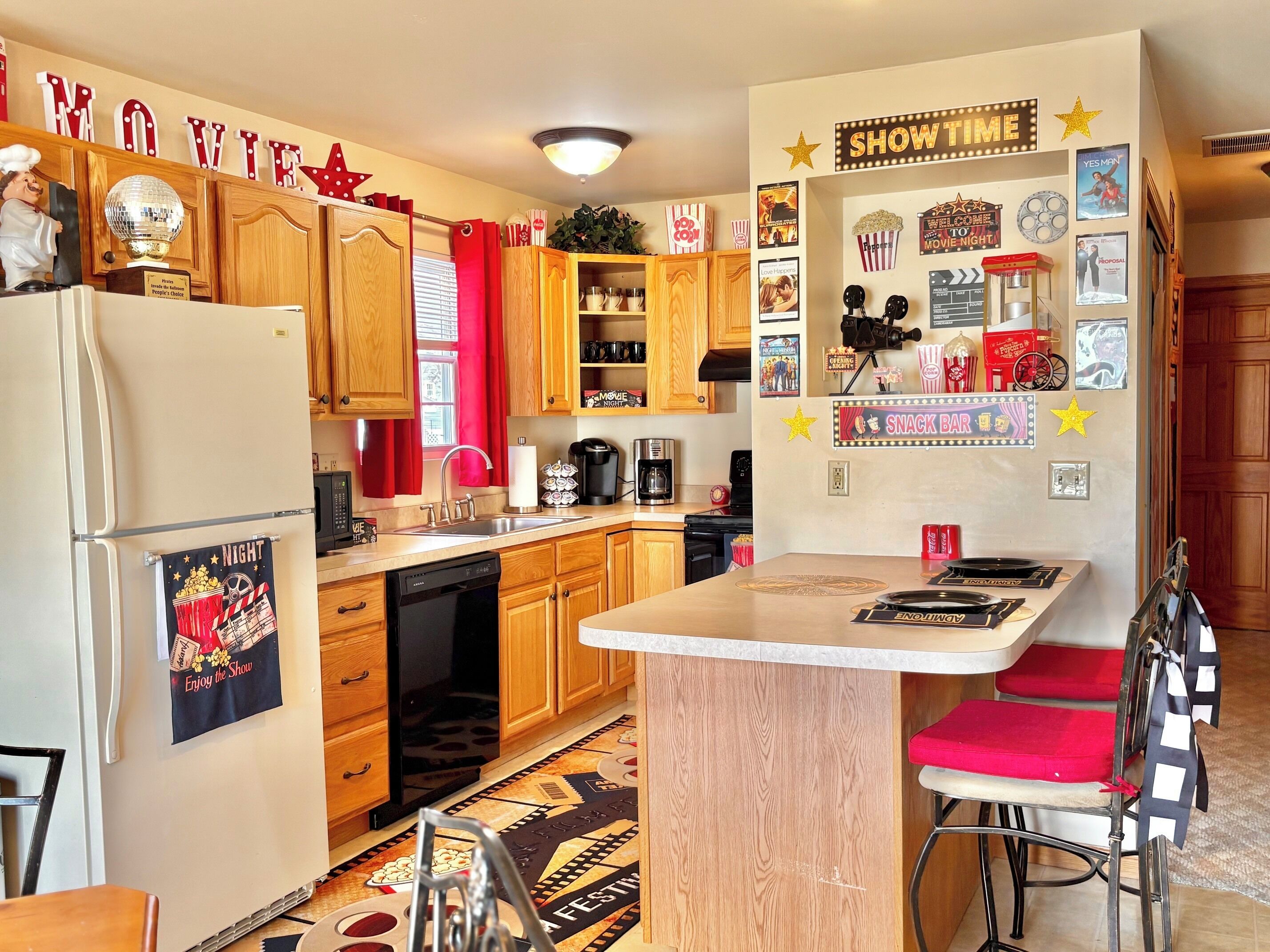 A kitchen with wooden cabinets, a refrigerator, a sink, and a bar area with a red chair.