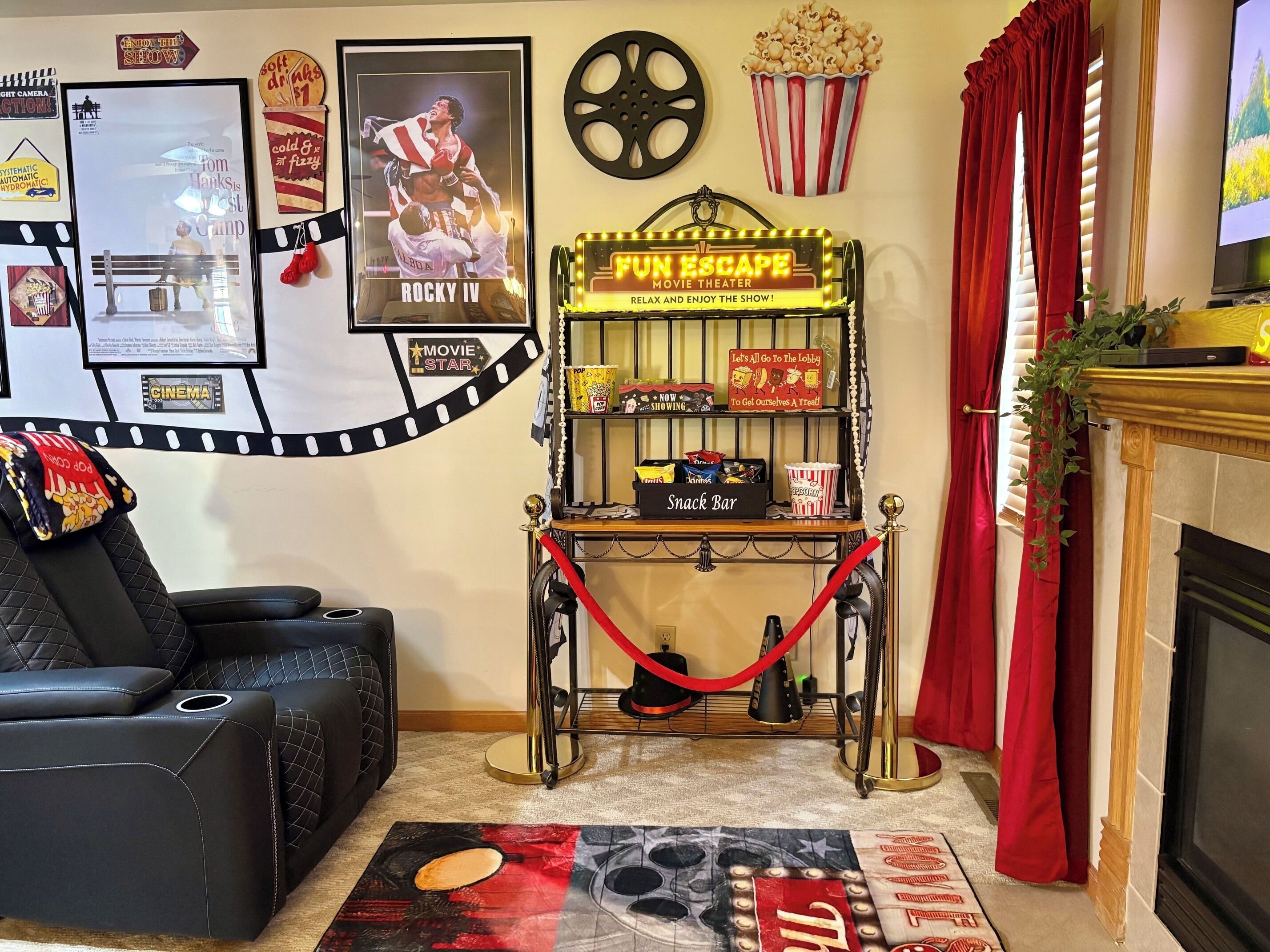 A cozy living room with a black leather sofa, a red curtain, a fireplace, a snack bar, and movie theater-themed decorations.