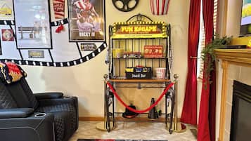 A cozy living room with a black leather sofa, a red curtain, a fireplace, a snack bar, and movie theater-themed decorations.