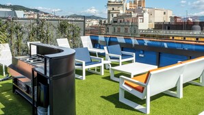 An outdoor seating area with a grill, white and orange chairs, and a view of the cityscape. - Designer Apart •High Floor Fast WiFi, Sagrada (Barcelona)