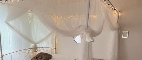 A bed with a canopy, a bedside table, and a wall-mounted picture frame.