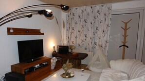 A living room with a television, a coffee table, a white sofa, a wooden cabinet, and a tent-like structure.