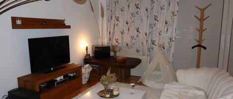 A living room with a television, a coffee table, a white sofa, a wooden cabinet, and a tent-like structure.