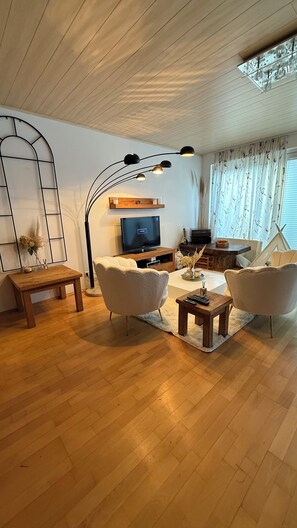 Un salón moderno con suelo de madera, televisor, sofá, mesa de centro y lámpara.