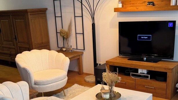 A modern living room with a white sofa, a white armchair, a coffee table, a TV, and a wooden cabinet.