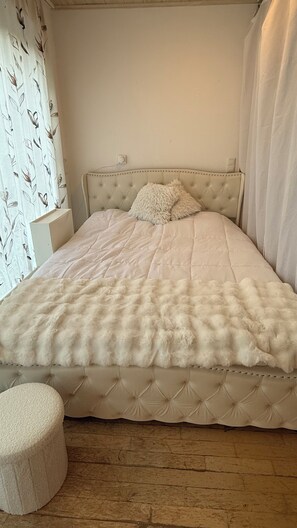 A bed with a tufted headboard, a fluffy white bedspread, and a matching ottoman.