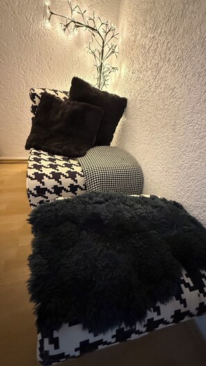 Una habitación con cama, una manta suave de pelo negro y una planta sujeta a la pared.