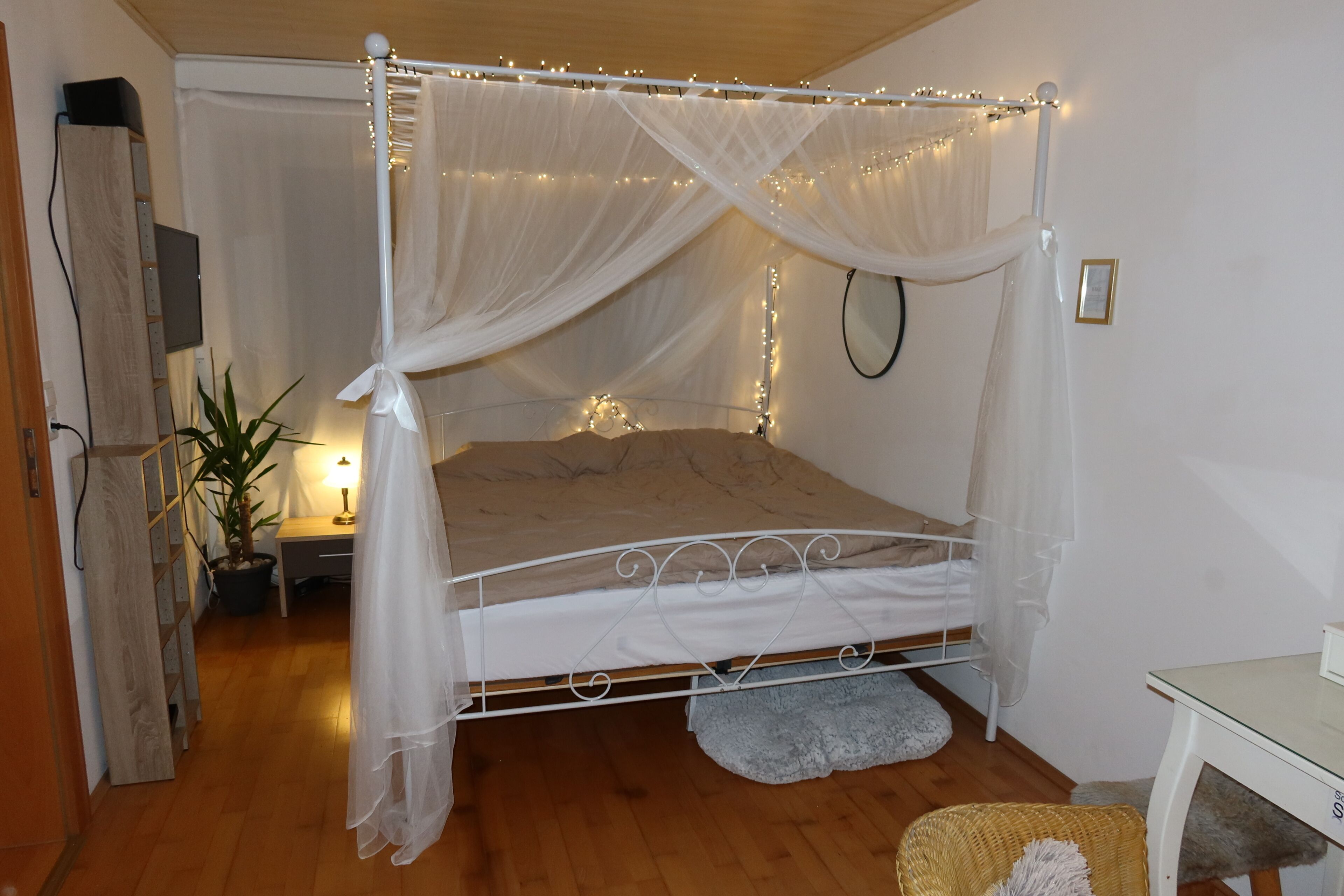 A four-poster bed with a canopy, a bedside table with a lamp, and a small potted plant.