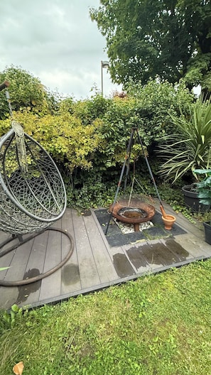 A garden with a swing chair, a birdbath, and a wooden deck.