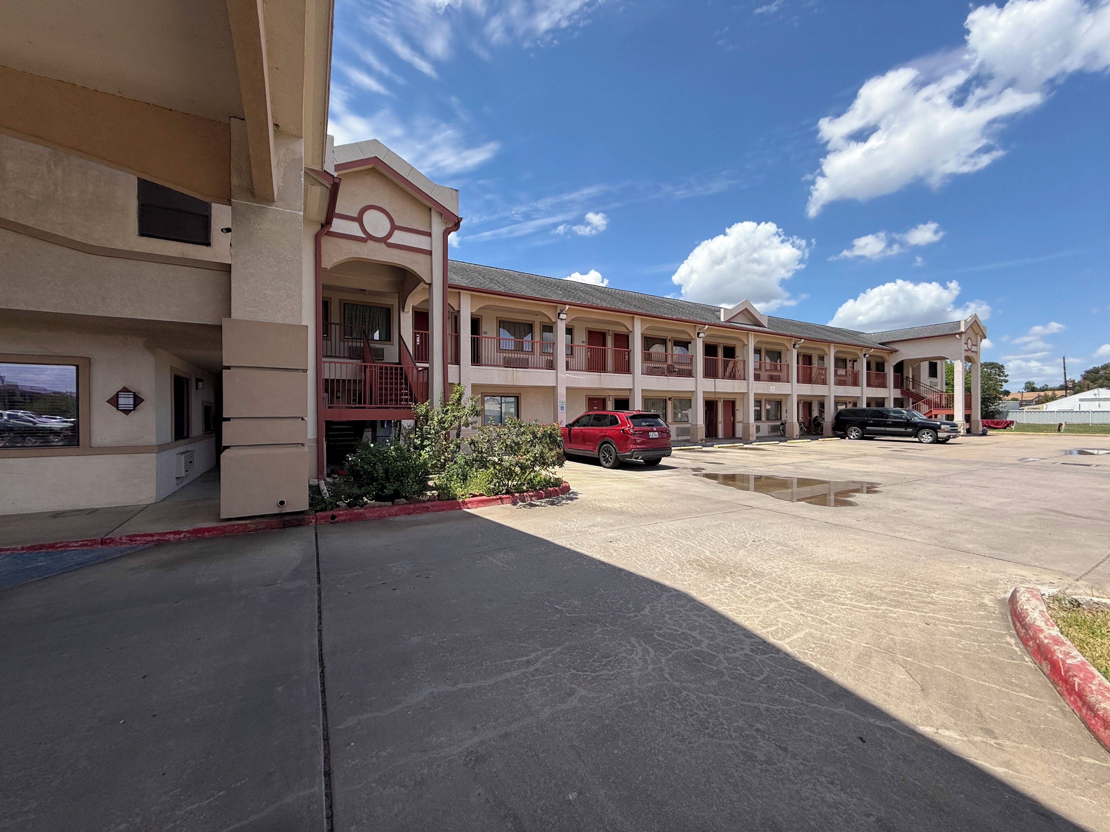 A multi-story motel with a central courtyard, outdoor parking, and a clear sky.