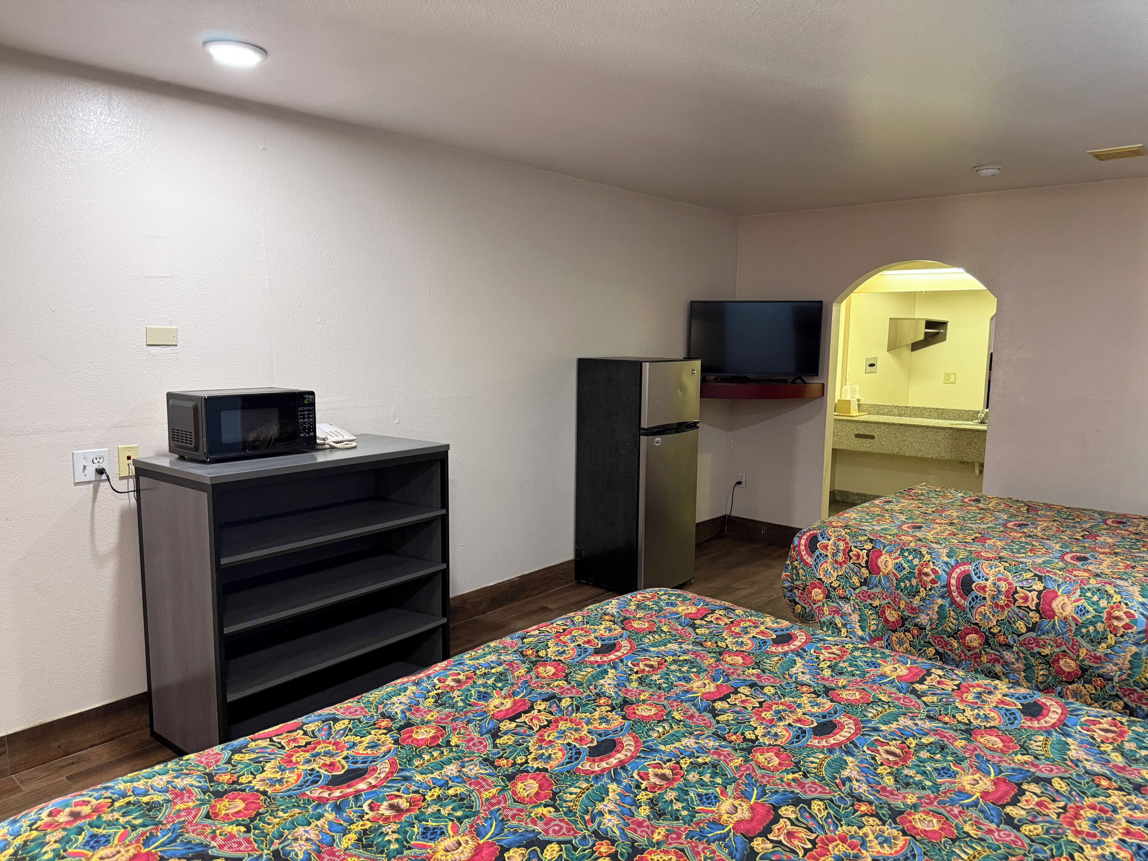 A room with two beds, a microwave, a refrigerator, a television, and a small kitchenette.