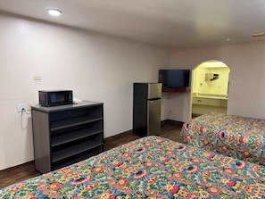 Una habitación con dos camas, microondas, refrigerador, televisor y una pequeña kitchenette.