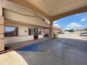 A hotel entrance with a covered walkway, a parking lot, and a clear sky.