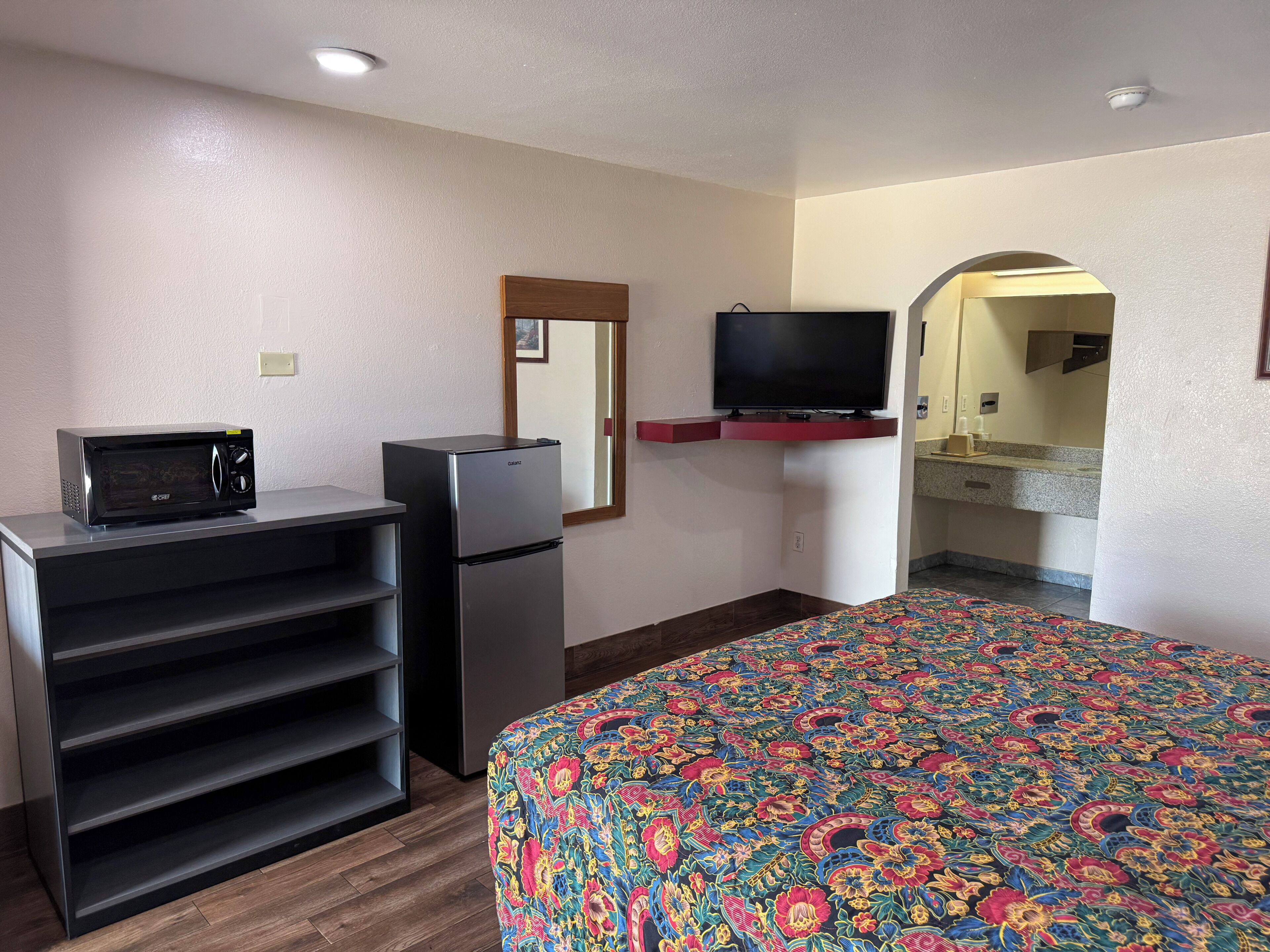 A hotel room with a bed, a refrigerator, a microwave, a television, and a small desk.