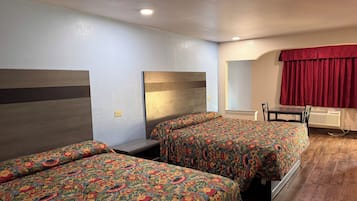 Ein Hotelzimmer mit zwei Betten, einem kleinen Tisch, einem Stuhl und einem Fenster mit roten Vorhängen.