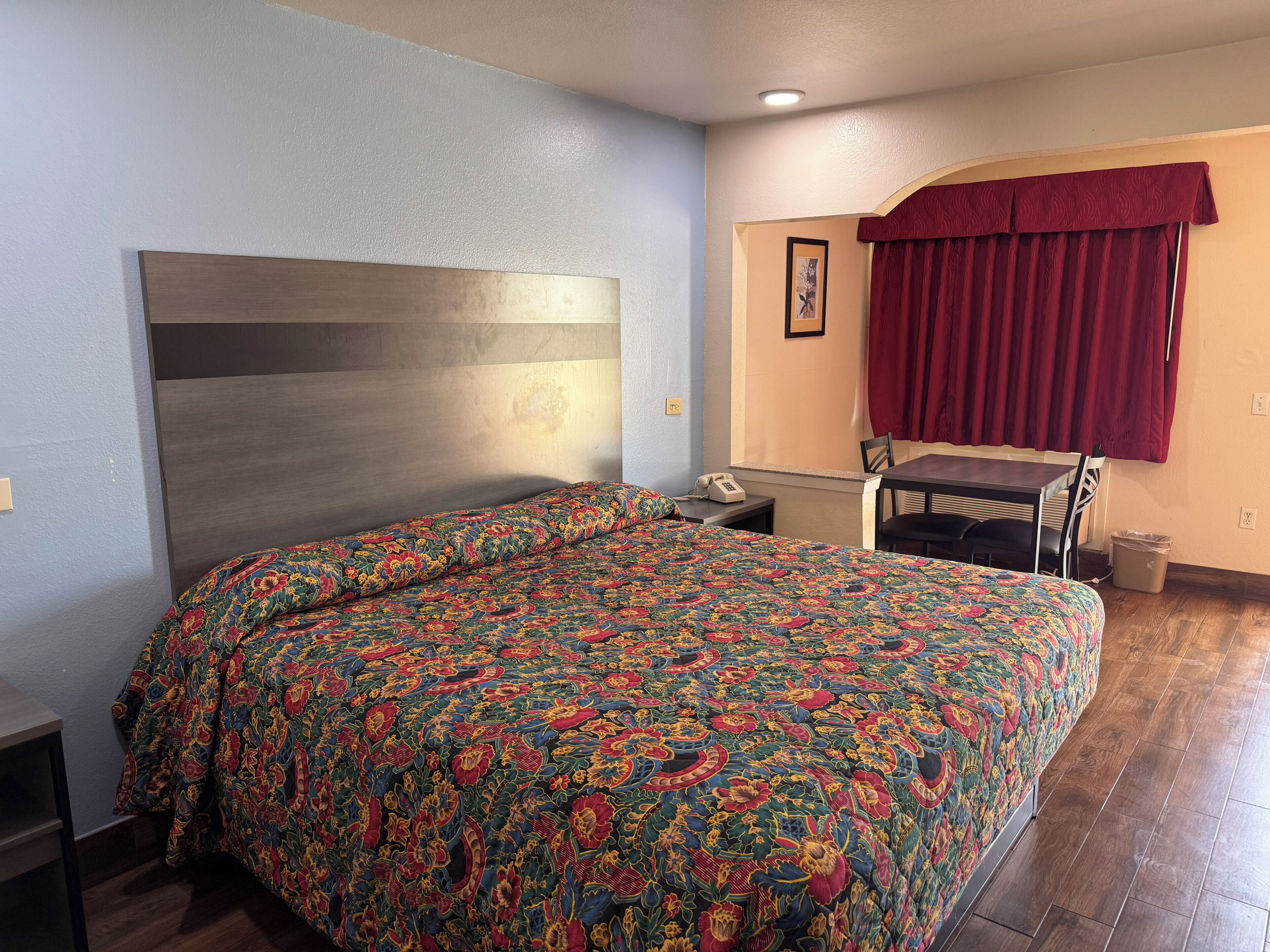 A hotel room with a bed, a desk, a chair, a telephone, and a window with curtains.
