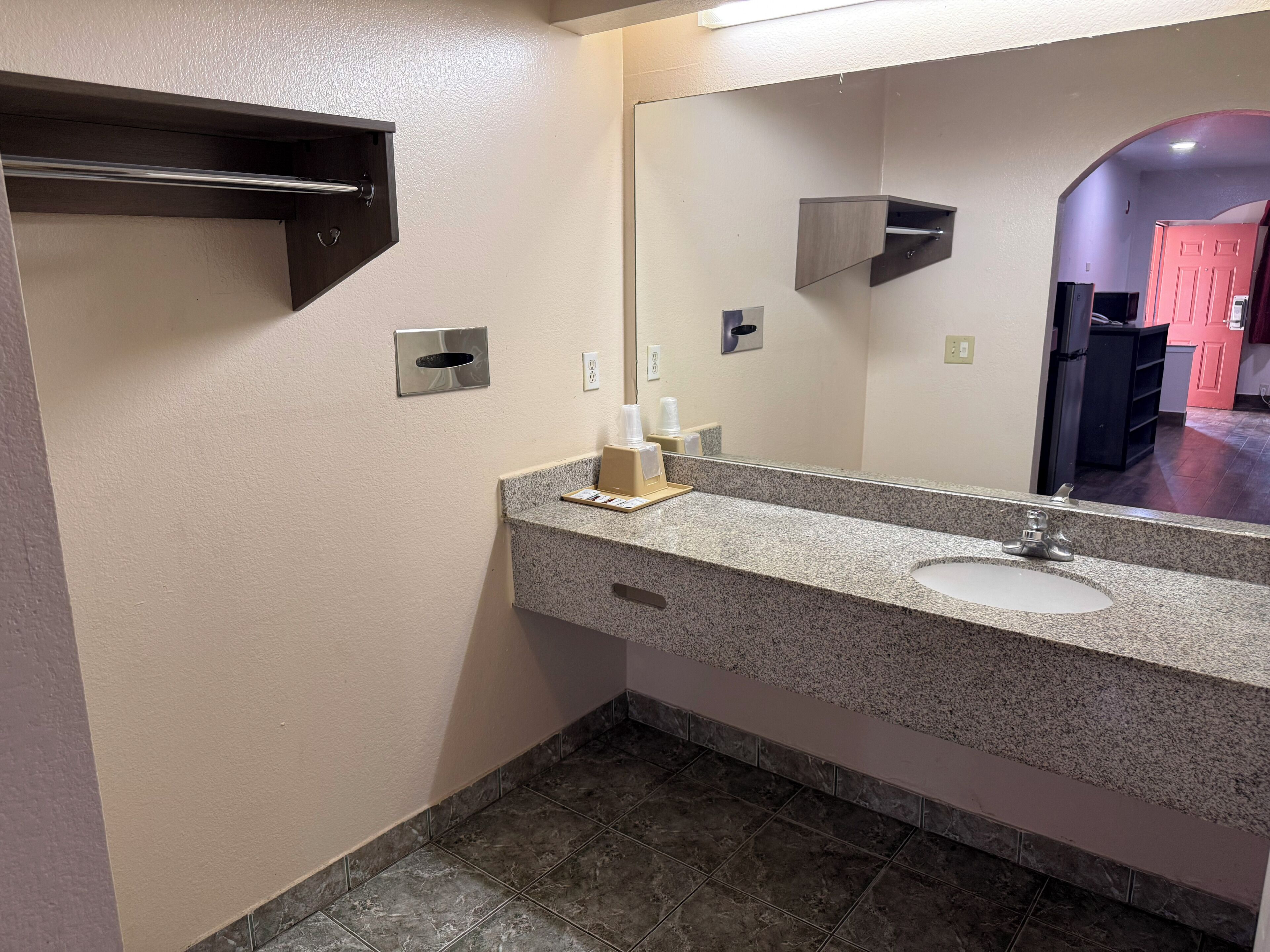 A bathroom with a granite countertop, a sink, a mirror, and a towel dispenser.