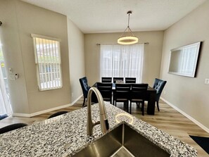 A modern kitchen with granite countertops, stainless steel sink, and a dining area with a table and chairs. - Tuscan Hills 5BR Villa | Private Pool & Spa (Davenport)
