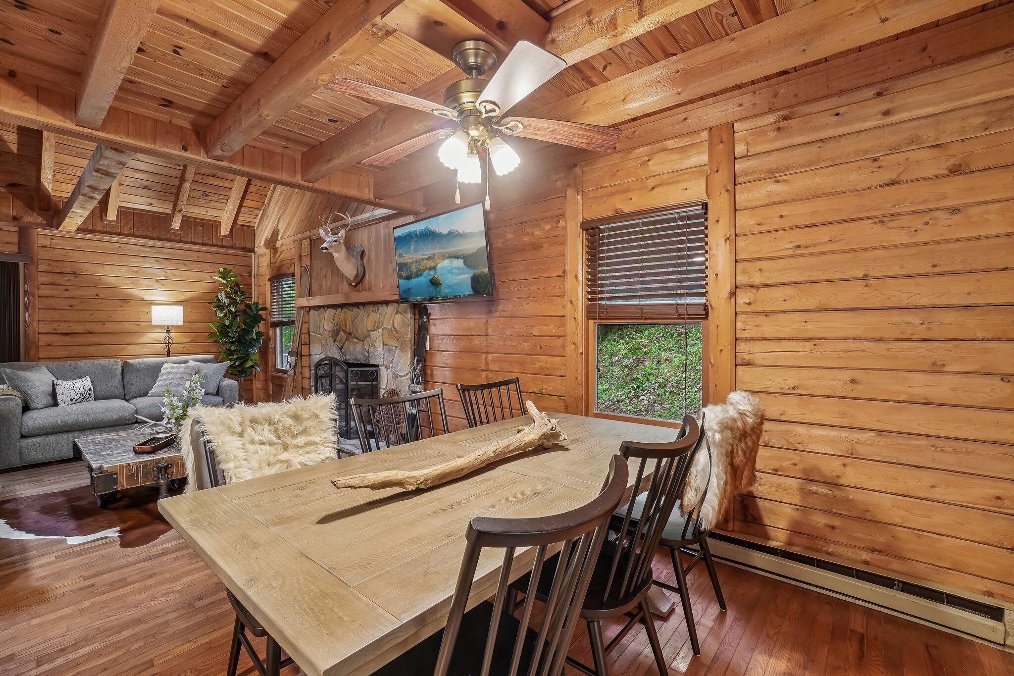 L’intérieur chaleureux d’un chalet comprend une table à manger, des chaises, une cheminée et un téléviseur fixé au mur.