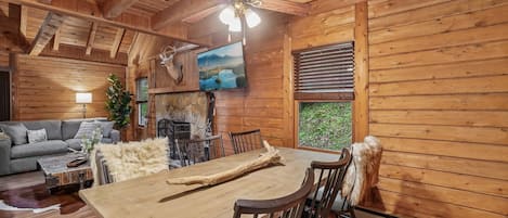L’intérieur chaleureux d’un chalet comprend une table à manger, des chaises, une cheminée et un téléviseur fixé au mur.