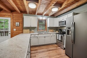 A kitchen with wooden beams, white cabinets, a stainless steel refrigerator, and a built-in oven. - Wolf Laurel Cabin with Hot Tub Near Skiing (Mars Hill)