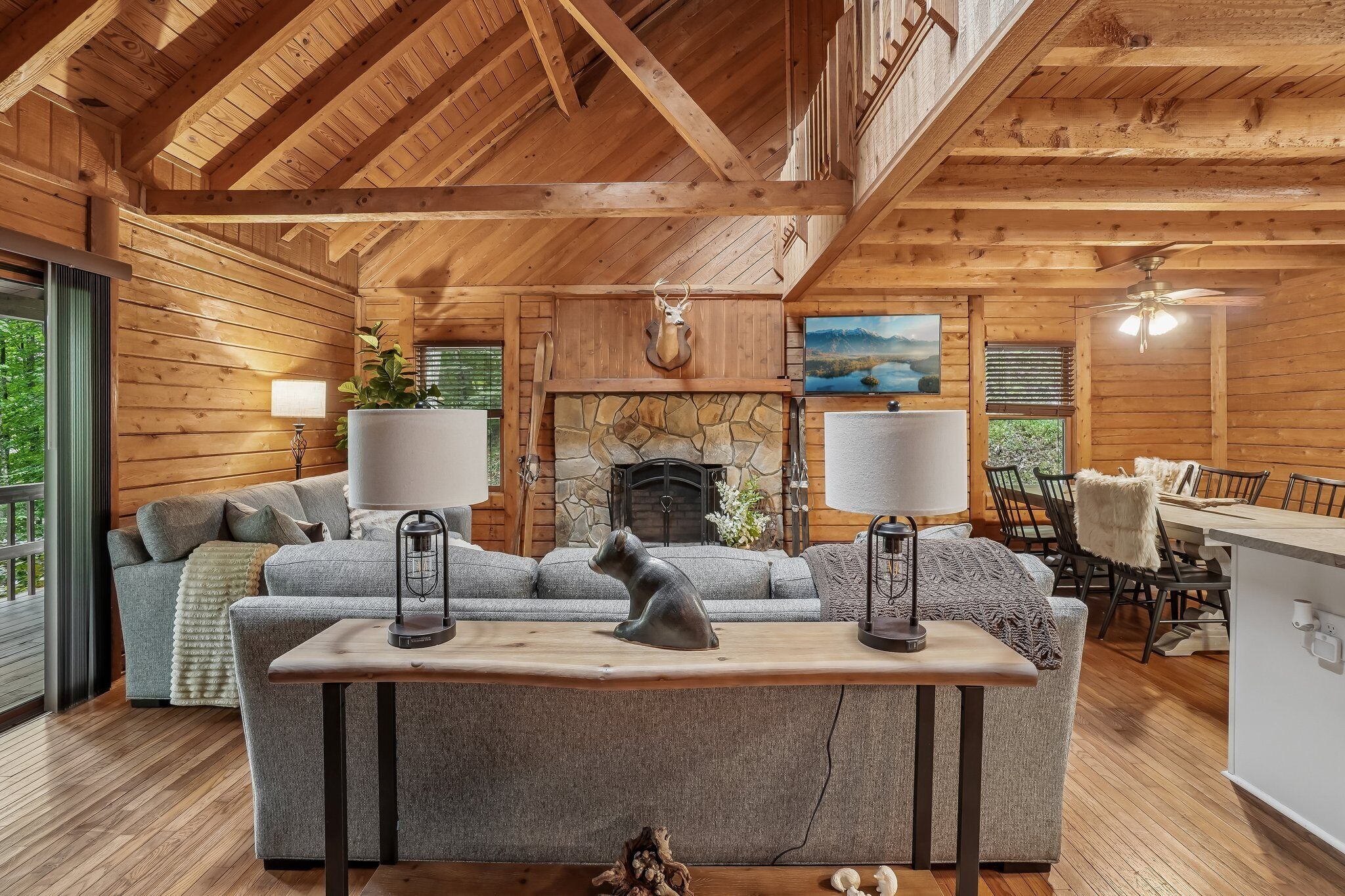 A cozy cabin interior with a fireplace, wooden walls, a sofa set, and a dining area.