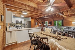 A wooden cabin interior with a kitchen, dining area, and living room. - Wolf Laurel Cabin with Hot Tub Near Skiing (Mars Hill)