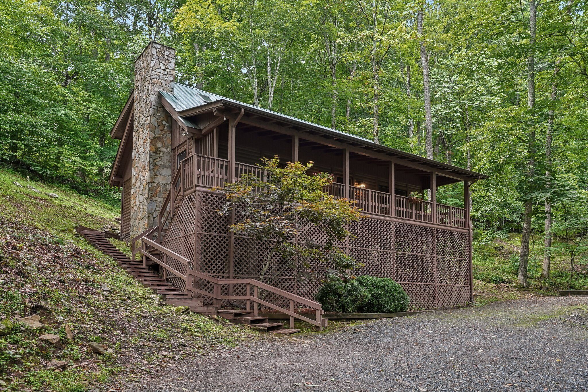 A cabin with a stone chimney, wooden deck, and a staircase leading to a porch.