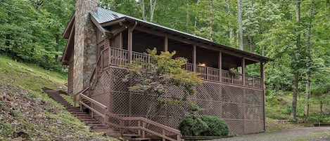 A cabin with a stone chimney, wooden deck, and a staircase leading to a porch.