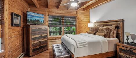 A wooden cabin bedroom with a bed, a bench, a television, and a window with blinds.