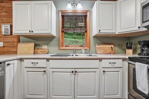 A kitchen with white cabinets, a window with blinds, a sink, and a stove. - Wolf Laurel Cabin with Hot Tub Near Skiing (Mars Hill)