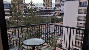 Un balcón con una mesa redonda y sillas, vista a un paisaje urbano con edificios modernos y un piso de baldosas.