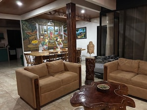 A living room with two sofas, a wooden coffee table, and a dining area with a mural. - Sonado Vacation Home for Large Groups (La Perla)