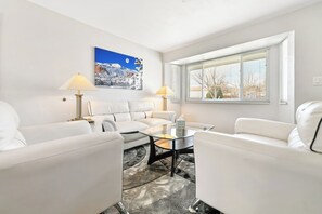 A modern living room with a white sofa set, a glass coffee table, and two lamps.