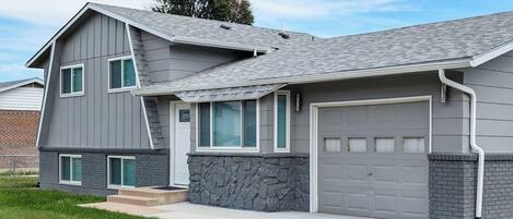 A two-story house with a garage, stone foundation, and a sloped roof.