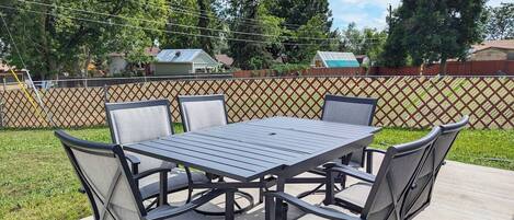Um pátio externo com mesa e cadeiras de metal, cercado por um portão de treliça.