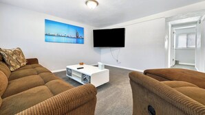 Ett modernt vardagsrum med en soffgrupp, ett soffbord, en platt-TV som är monterad på väggen och en tavla som föreställer en stadsbild.