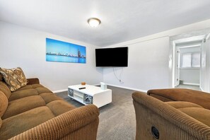 A modern living room with a sofa set, a coffee table, a flat-screen TV mounted on the wall, and a painting of a cityscape. - ᨒStylish 4BR | Movie Lounge | 10 min to Ft Carsonᨒ (Colorado Springs)
