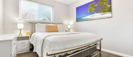 A bedroom with a bed, bedside lamps, a window, and a wall-mounted picture.