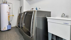 Ett tvättrum med en varmvattenberedare, två tvättmaskiner placerade ovanpå varandra och ett handfat.