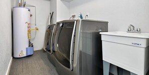 A laundry room with a water heater, two stacked washers, and a sink. - ᨒStylish 4BR | Movie Lounge | 10 min to Ft Carsonᨒ (Colorado Springs)