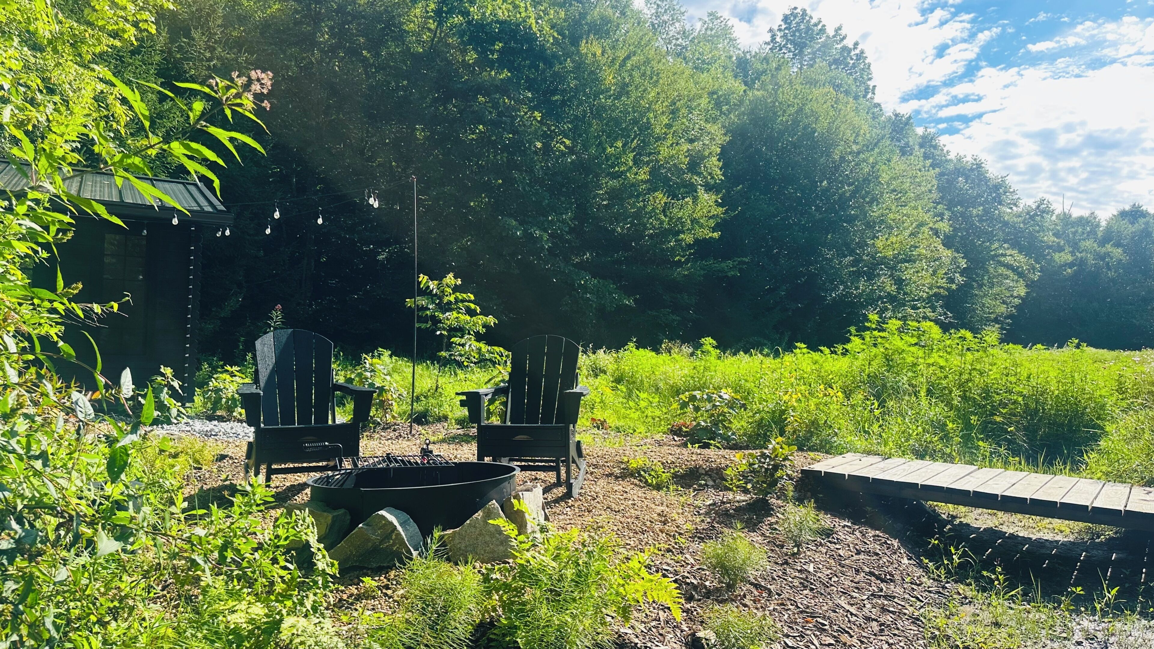 A garden area with two Adirondack chairs, a fire pit, and a wooden deck.