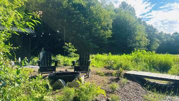 A garden area with two Adirondack chairs, a fire pit, and a wooden deck.